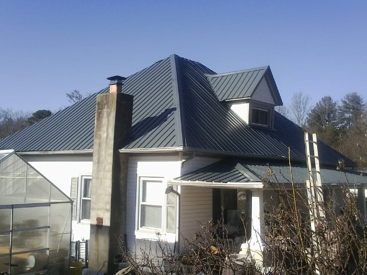 Dark blue standing seam metal roof on a white farmhouse with dormer — Slate & Tile Roof Repair by Roofing Brothers in Netawaka