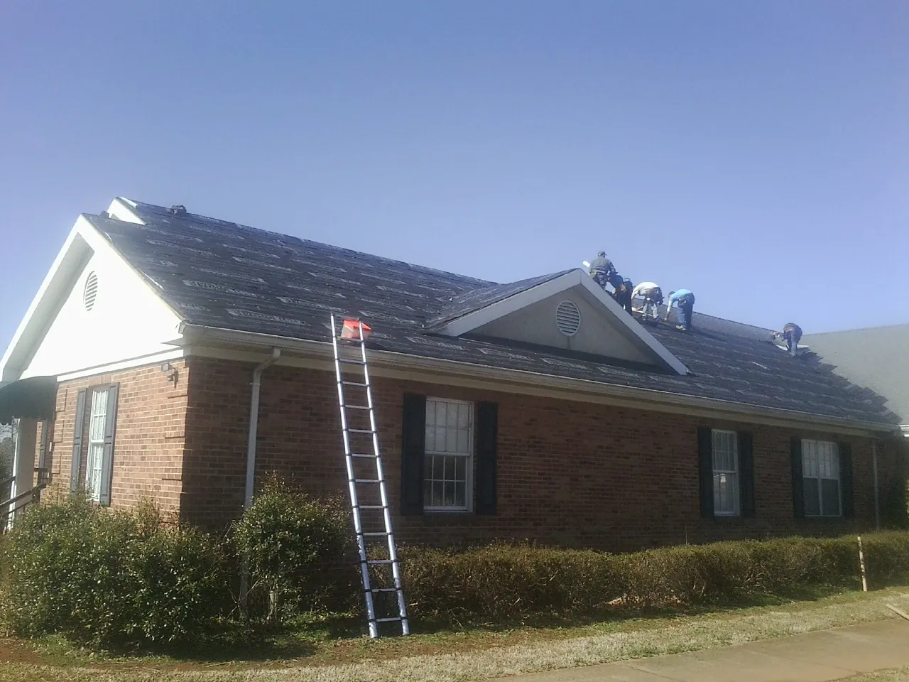 Crew tearing shingles off a brick ranch roof with a ladder set — Emergency Roof Repair work by our crew in Netawaka