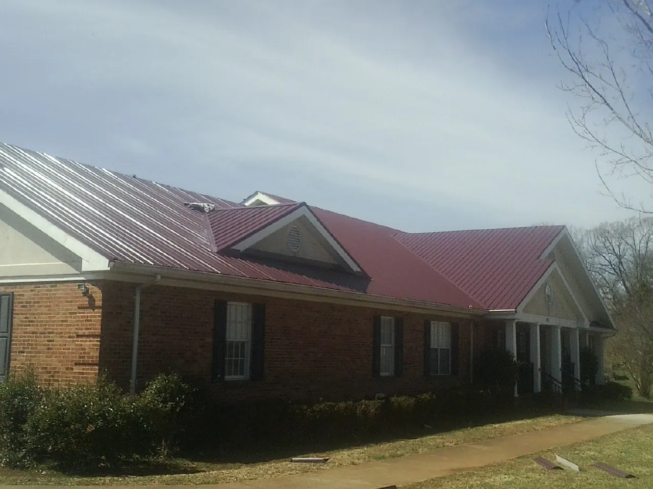 Red metal roof with gabled entries on a long brick building, from a Hail Damage Roof Repair job in Netawaka