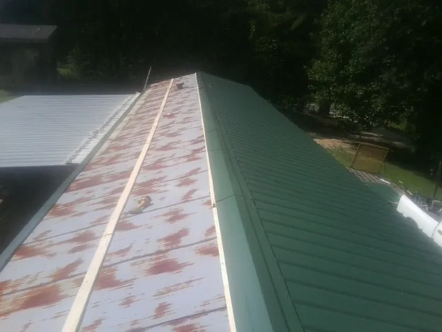 Old rusted panels beside newly installed green metal roofing — Wind Damage Roof Repair by Roofing Brothers in Netawaka