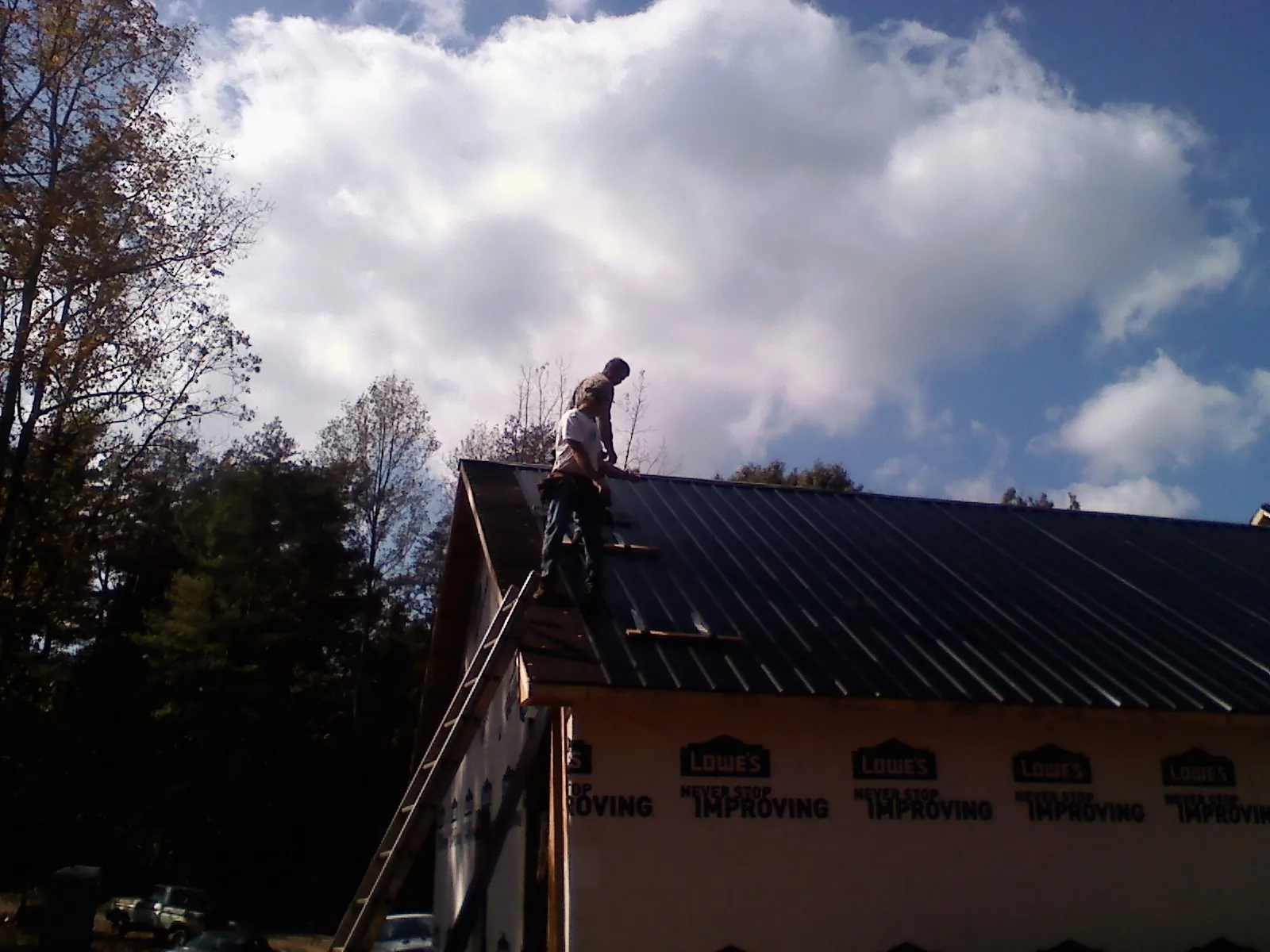 Roofer fastening dark metal panels high against a cloudy sky, from a Roof Inspection job in Netawaka