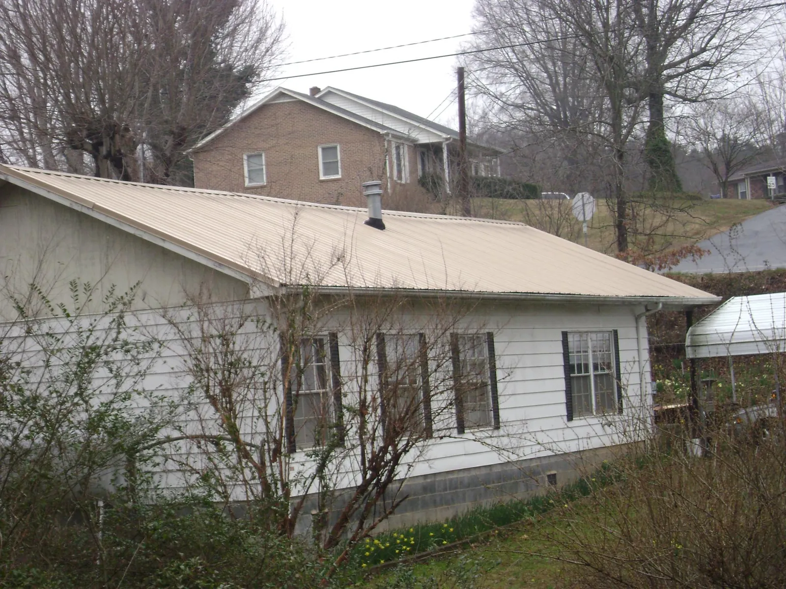 Tan metal roof on a white sided house set into a hillside — Commercial Roofing by Roofing Brothers in Netawaka